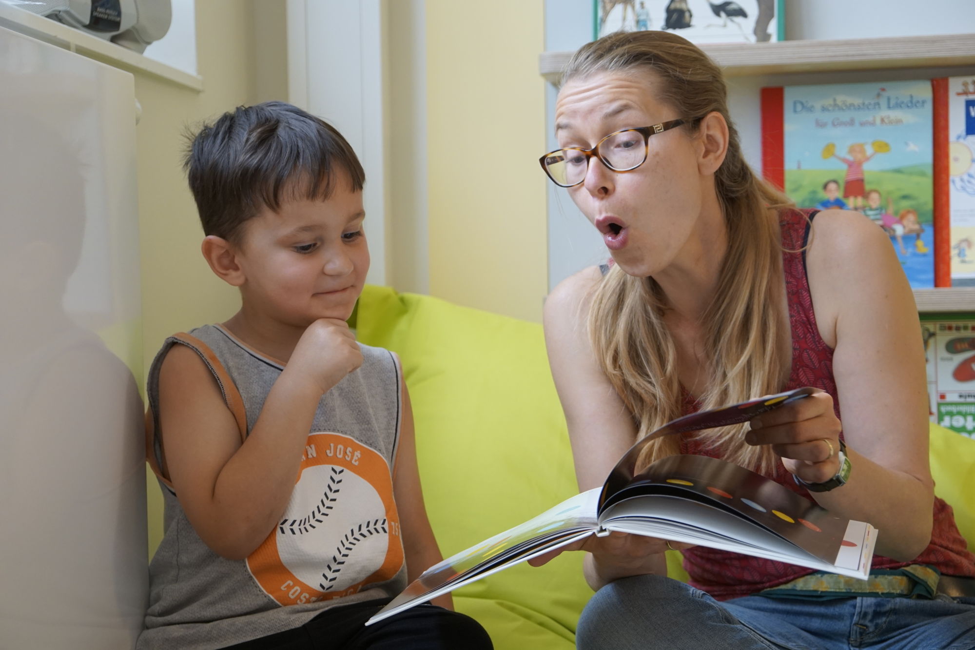 Eine Frau zeigt einem Kind ein Buch und formt den Mund zu einem großen O
