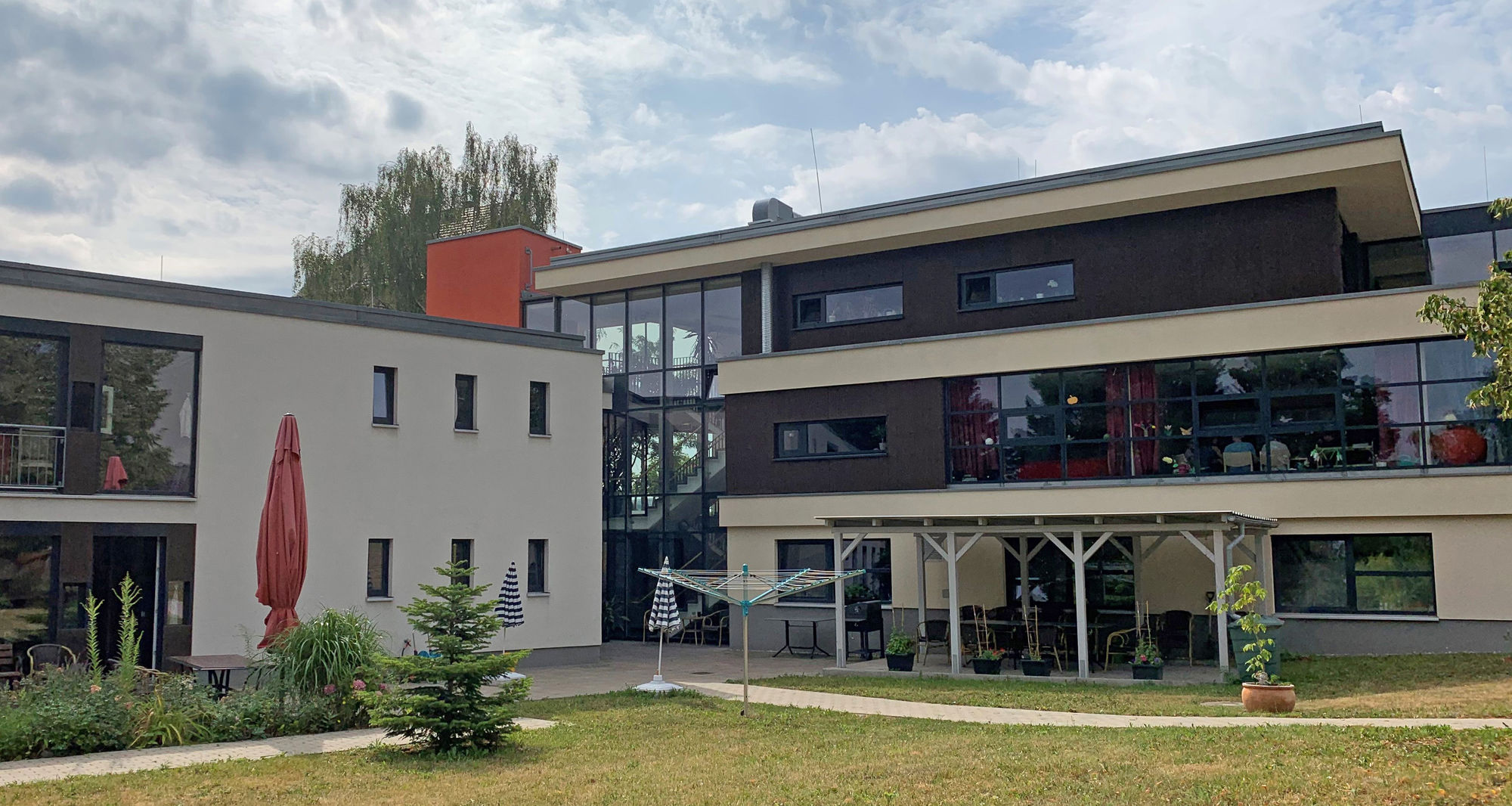 Ein großes Gebäude mit großen Fenstern, ein Garten und einer überdachten Terrasse