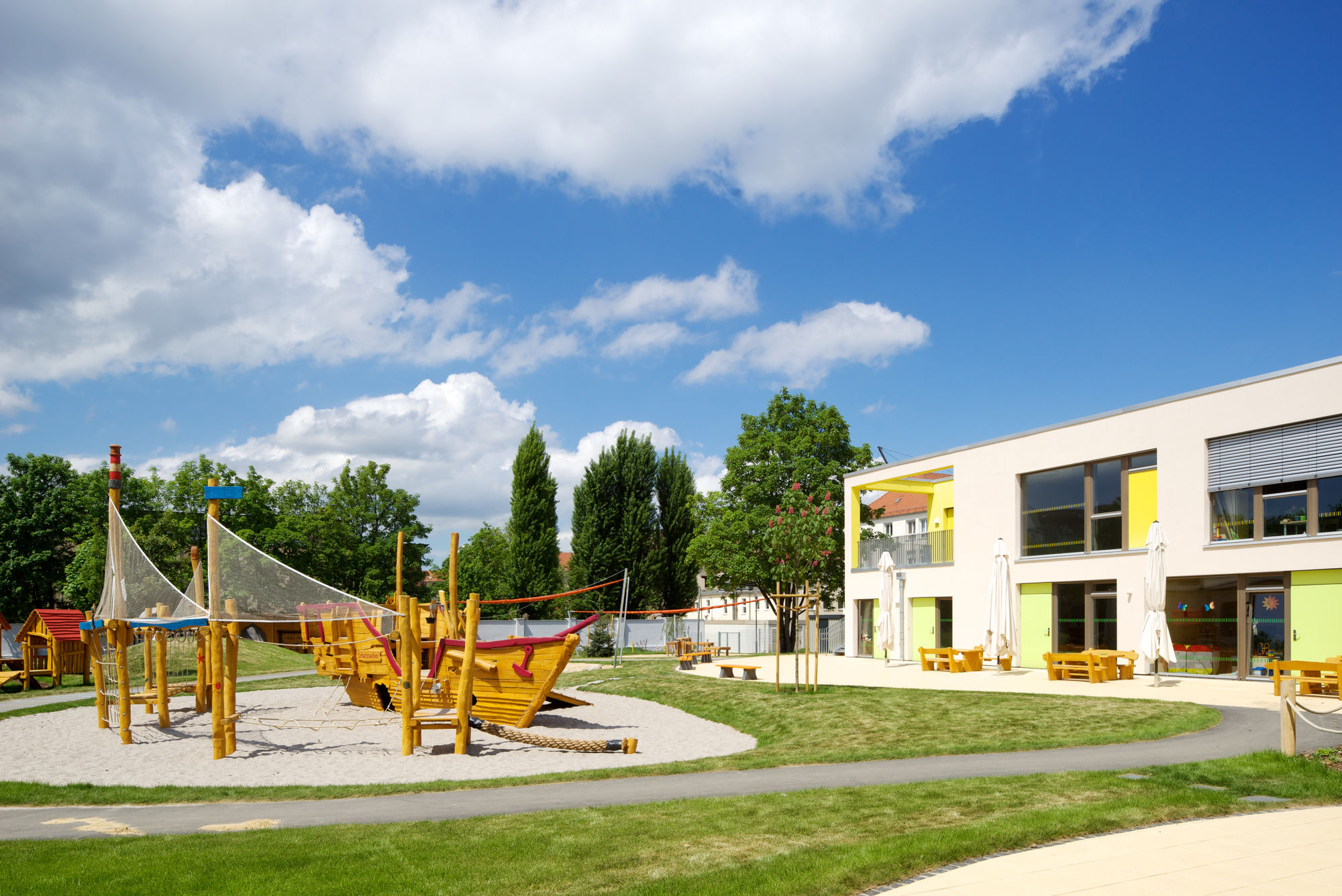 Ein großer Garten mit einem großen Kletter-Piratenschiff aus Holz, Wiesen, asphaltierten Fahrstrecken und Sandkästen.
