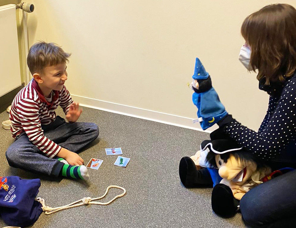 Eine Therapeutin zeigt eine Zauberer-Handpuppe einem lachenden Kind.